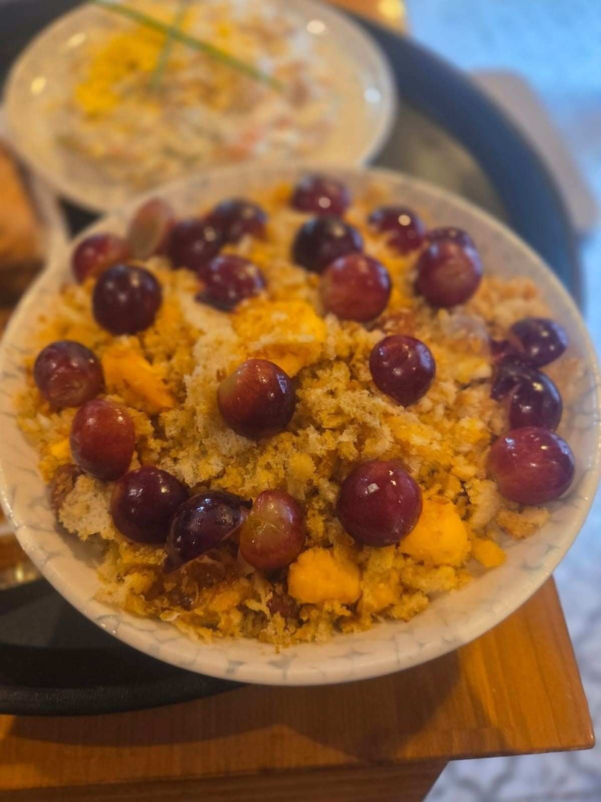 Cuenco de migas con uvas y trozos de naranja sobre una mesa.