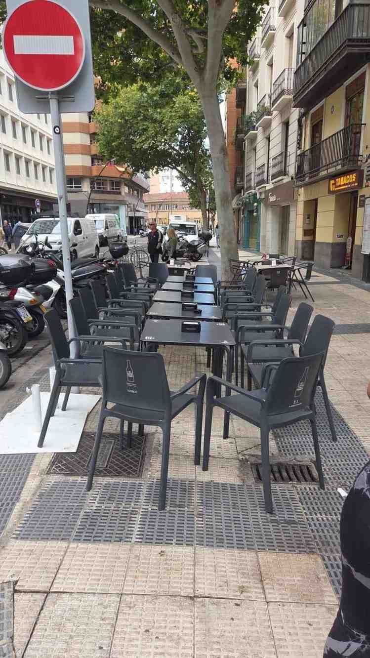 Cafetería al aire libre con mesas y sillas negras y un cartel de 