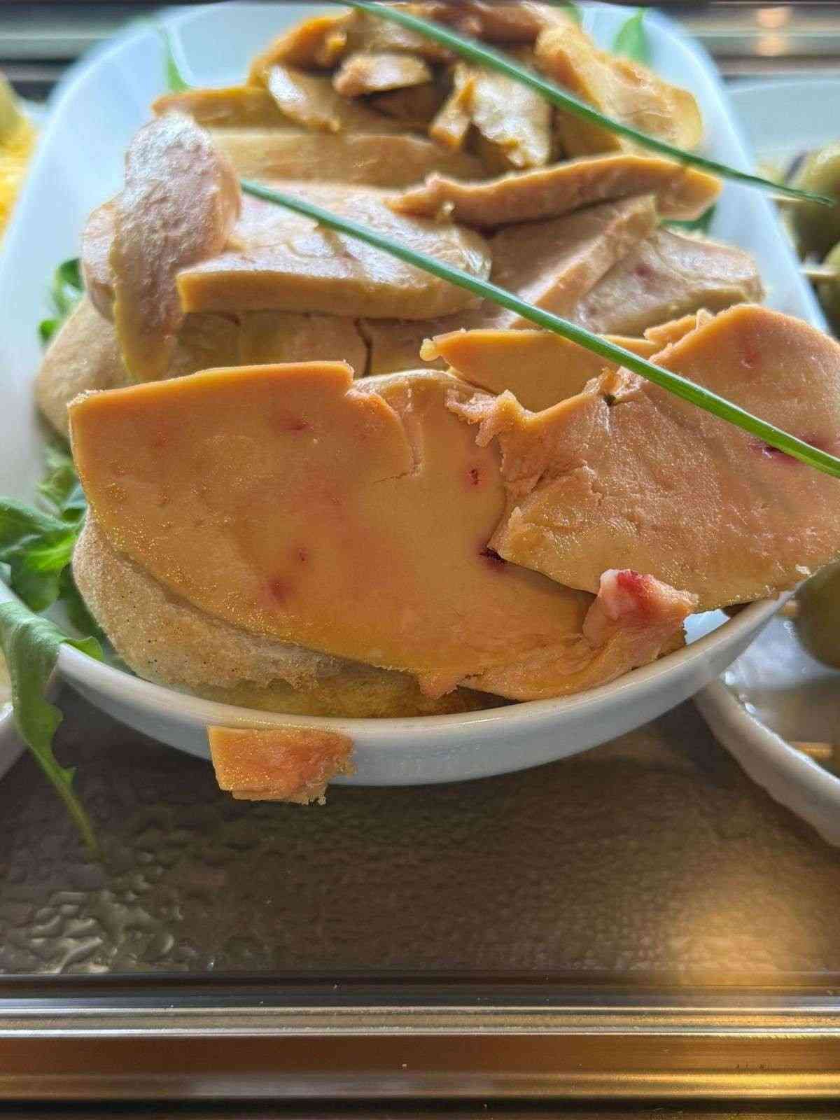 Foie gras en rodajas sobre pan, adornado con ramitas verdes, servido en un bol blanco.