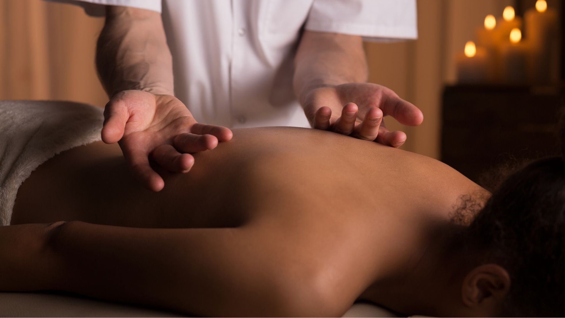 Las manos de una persona con uniforme blanco se ciernen sobre la espalda de una persona durante un masaje.