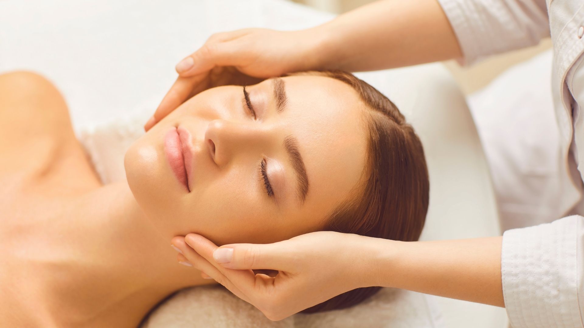 Mujer recibiendo un masaje facial con los ojos cerrados y las manos en la cara.