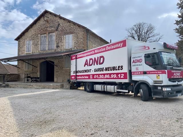 Camion de déménagement garé à côté d’un bâtiment en pierre, avec une grande enseigne rouge ADND sur le côté