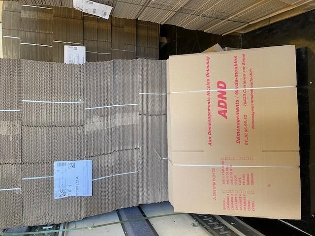 Des cartons empilés et des plaques de carton ondulé à plat dans un entrepôt, avec un carton beige portant l’inscription « ABCD »