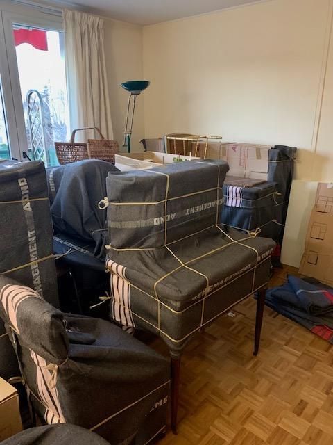 Salon encombré de meubles emballés dans des couvertures de déménagement foncées, avec des cartons empilés à proximité