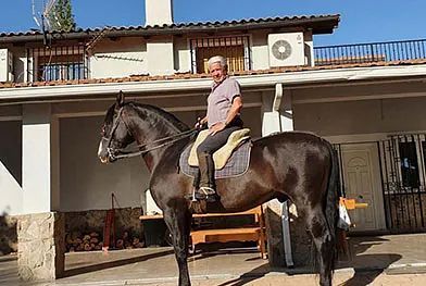 Un hombre está montando a caballo frente a una casa.