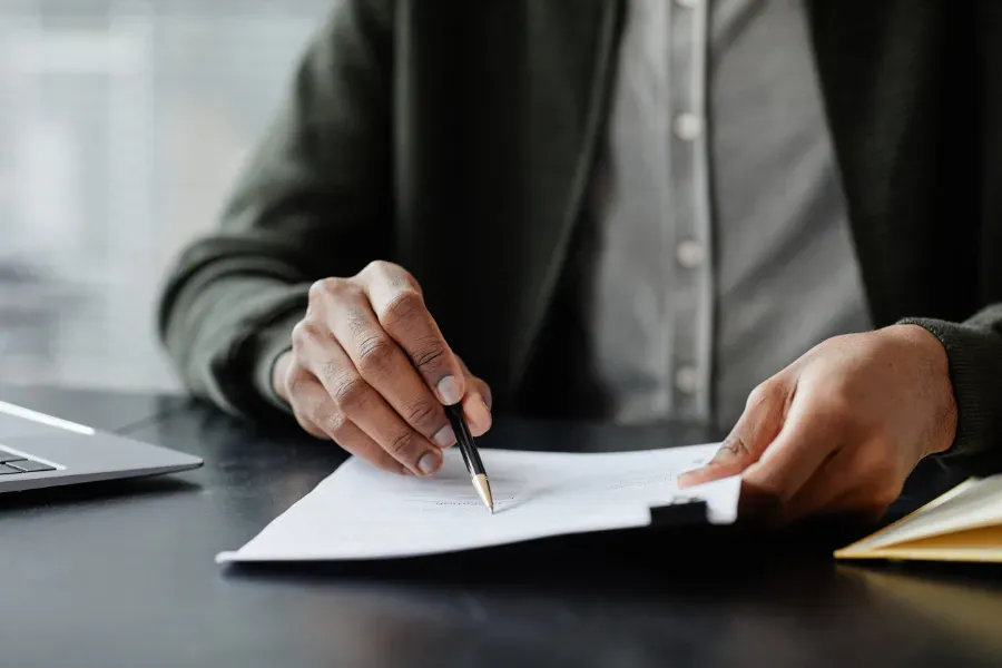 Persona vestida de traje firmando un documento en un escritorio con un bolígrafo.