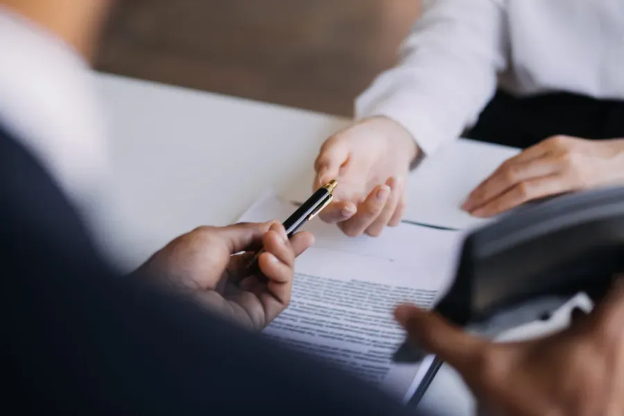 Manos intercambiando bolígrafos sobre documentos en un escritorio durante una reunión de negocios.
