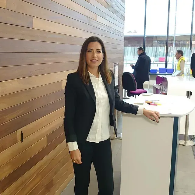 Una mujer con traje está parada frente a una pared de madera.