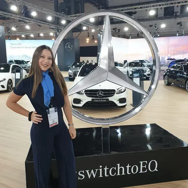 Una mujer está parada frente a un logotipo de Mercedes.