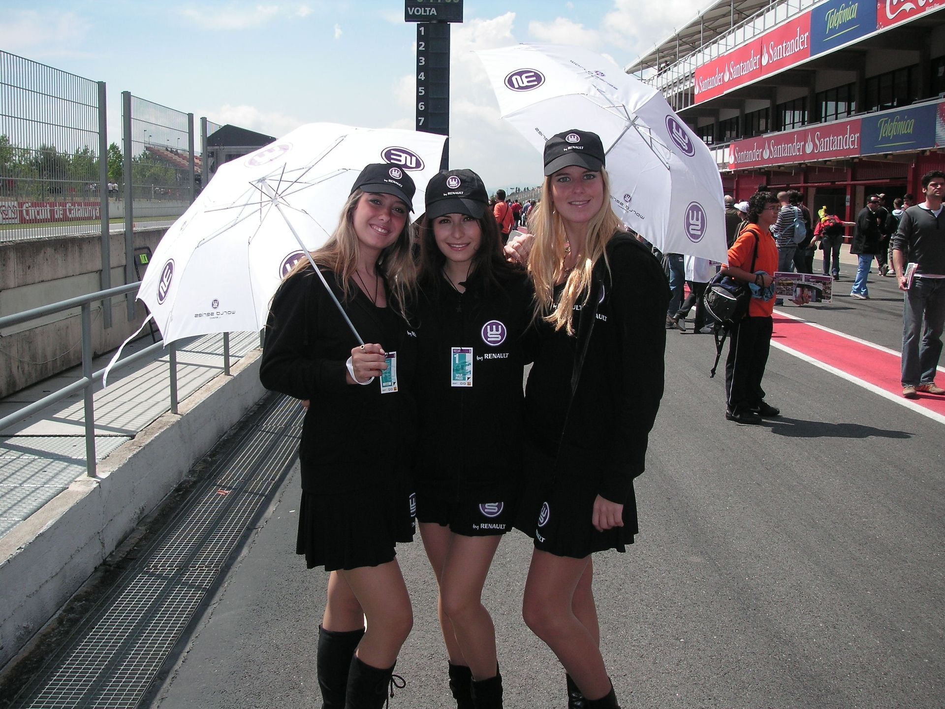 Tres mujeres sosteniendo paraguas frente a una pista de carreras