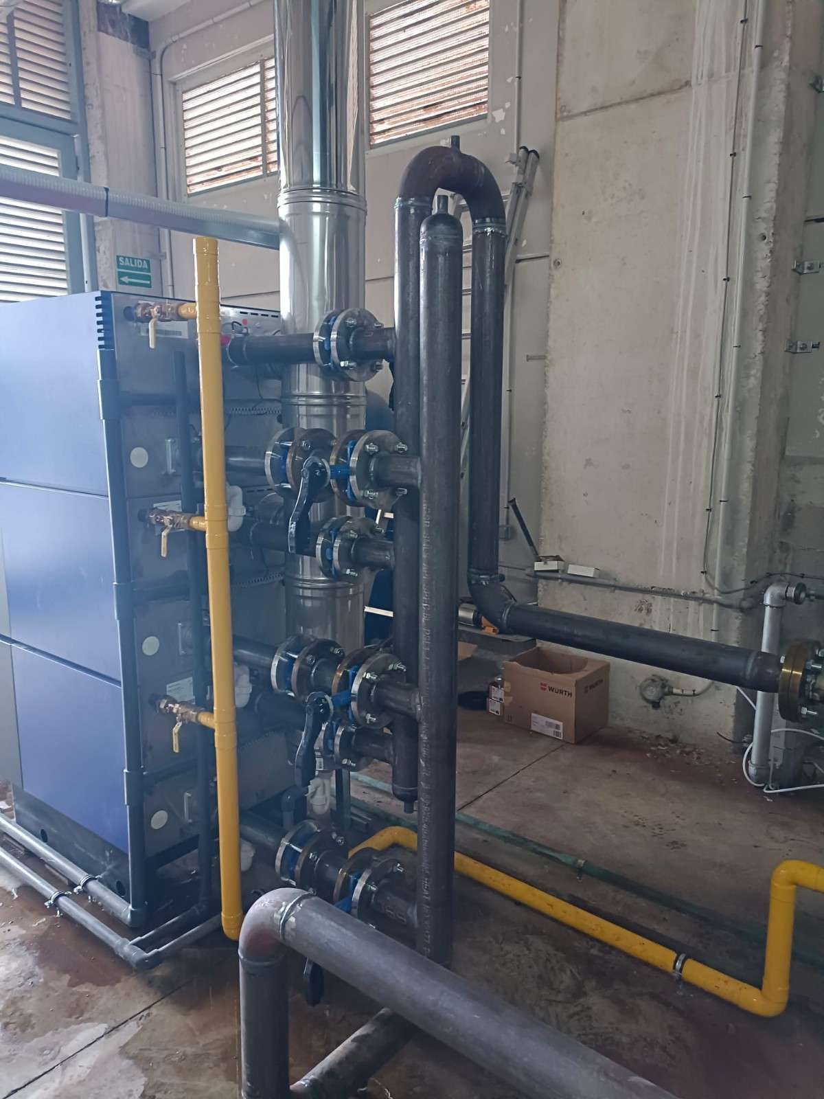 Equipo industrial con maquinaria, tuberías y válvulas azules en una sala de fábrica.