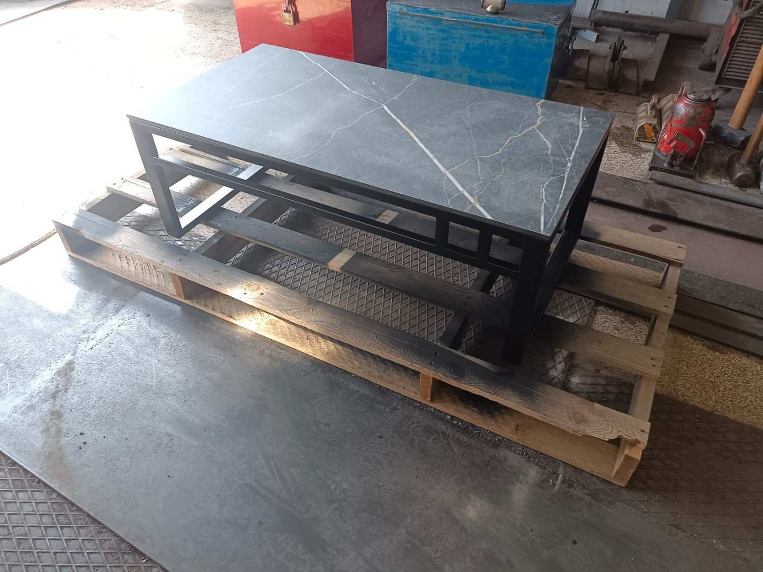 Mesa rectangular negra sobre palets de madera apilados en un taller.