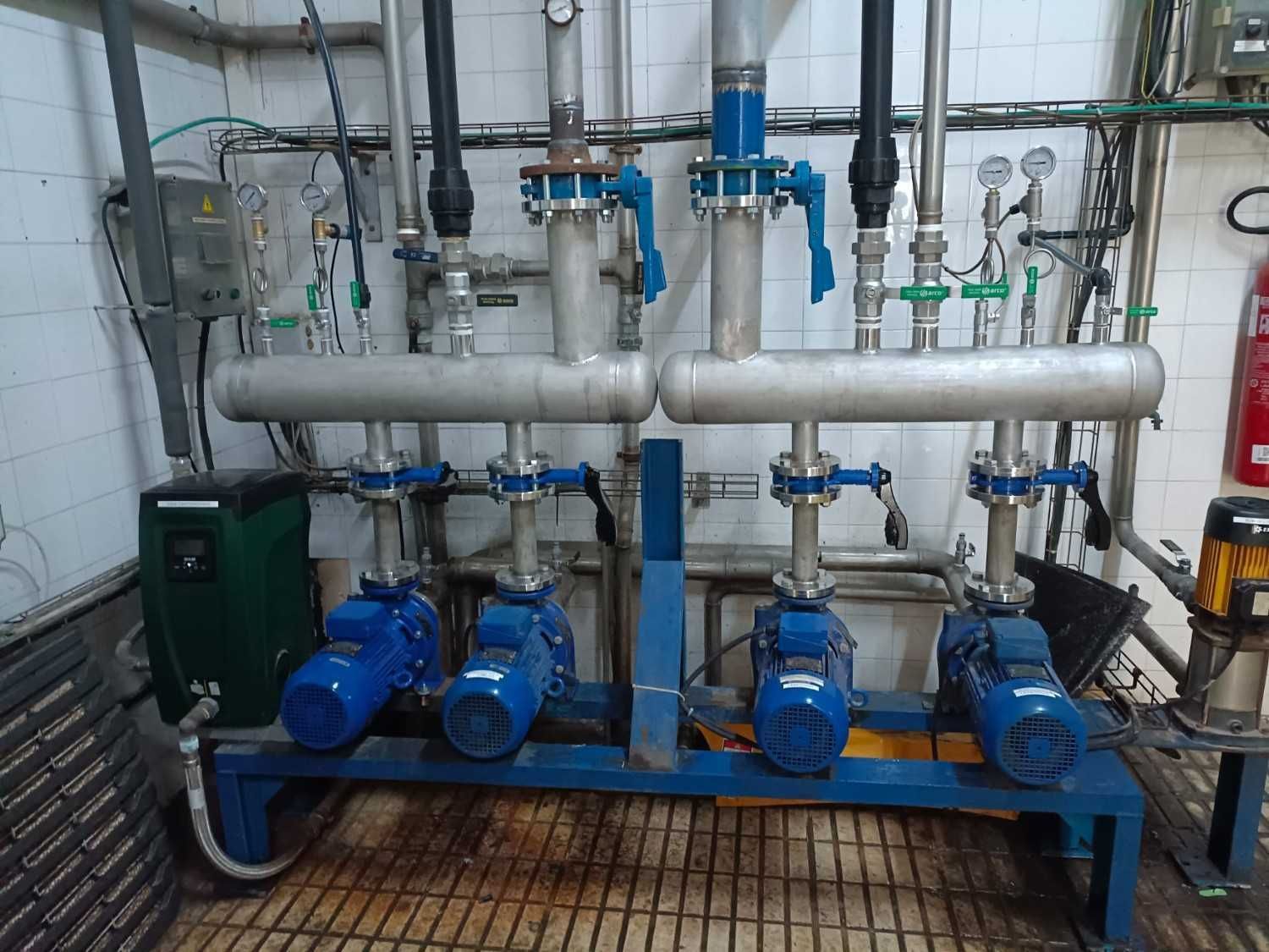 Bombas y tuberías industriales de color azul en una sala de máquinas con manómetros y válvulas conectadas.