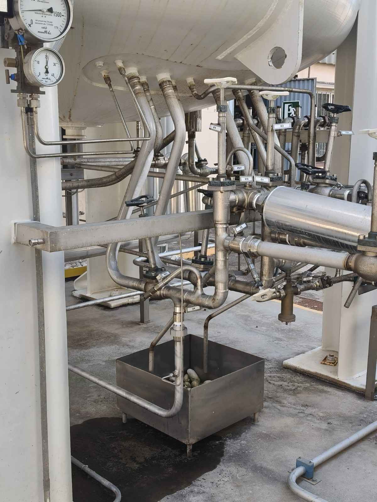 Tuberías y manómetros industriales sobre una bandeja de recogida metálica en un entorno de fábrica.