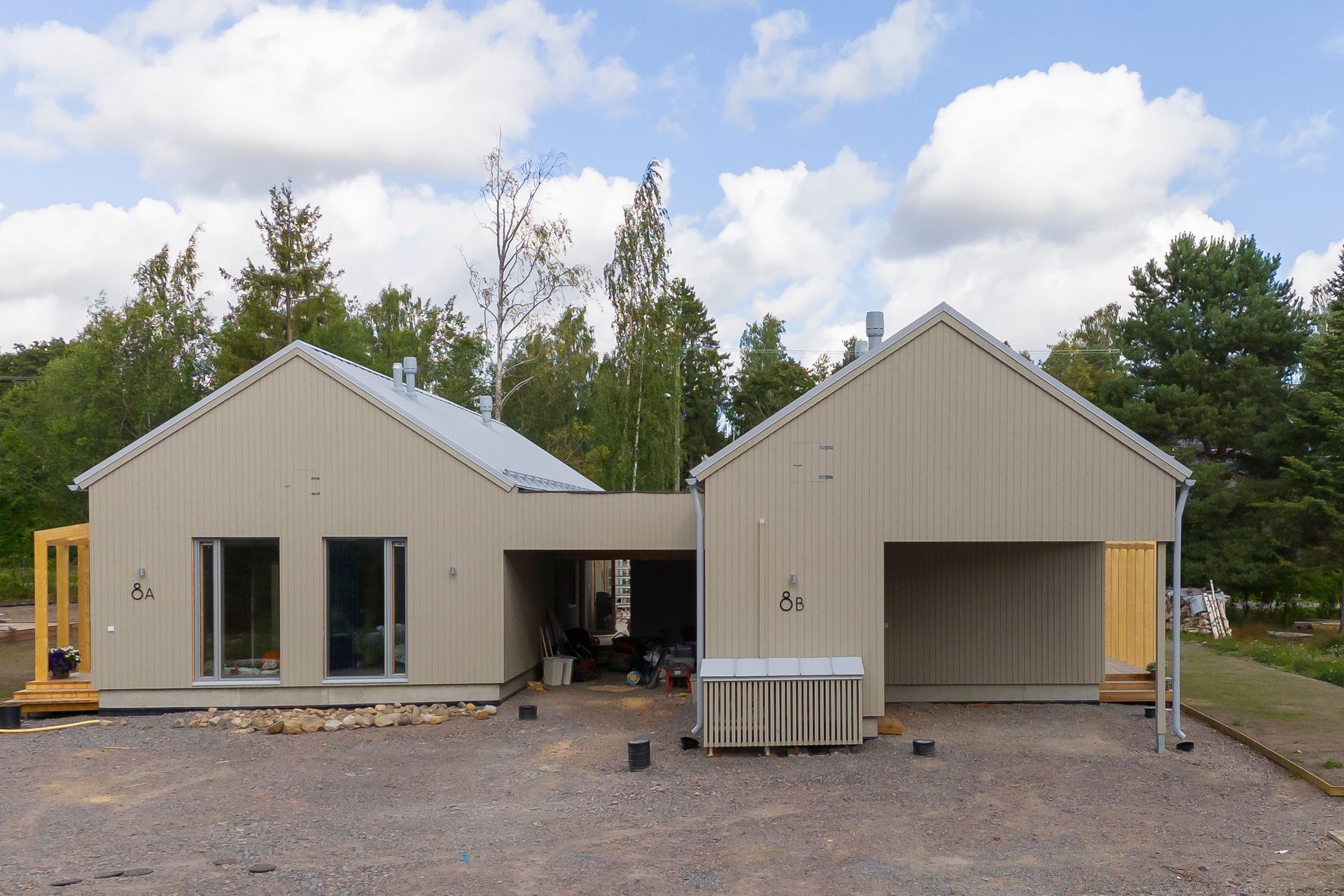 Kaksi pientä vaaleanbeigeä harjakattoista taloa sorapihalla pilvisen taivaan alla