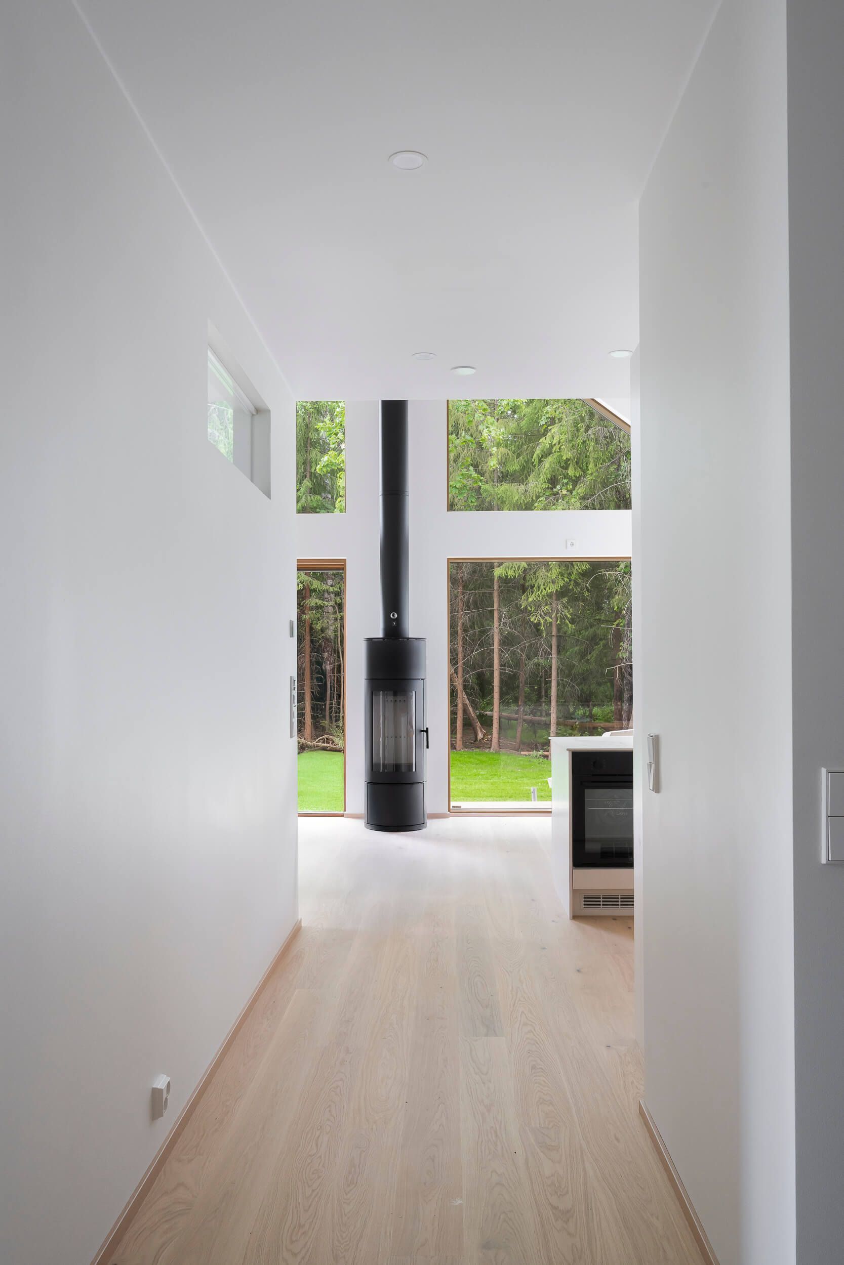 Valoisa käytävä, jossa on valkoiset seinät ja puulattiat, johtaa kohti korkeaa, sylinterinmuotoista takkaa ja ulkoilmanäkymää.