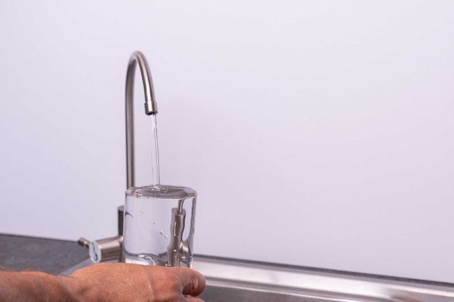 Una persona está vertiendo agua de un grifo en un vaso.