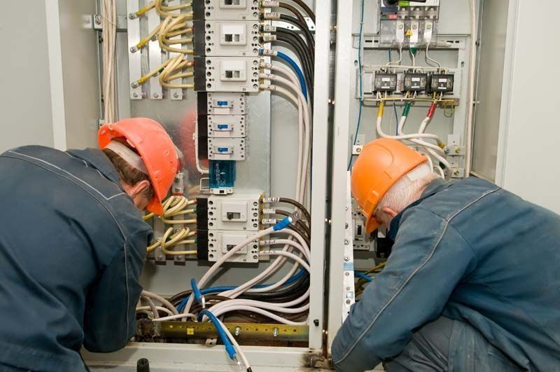 Dos hombres que llevan cascos están trabajando en una caja eléctrica.