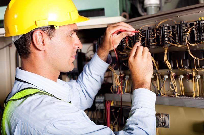 Un hombre que lleva un casco está trabajando en una caja eléctrica.