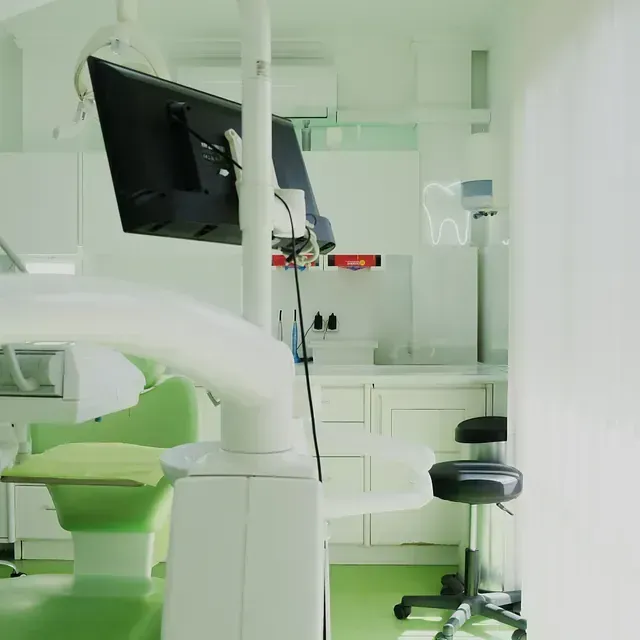 Un consultorio dental con una silla verde y un monitor.