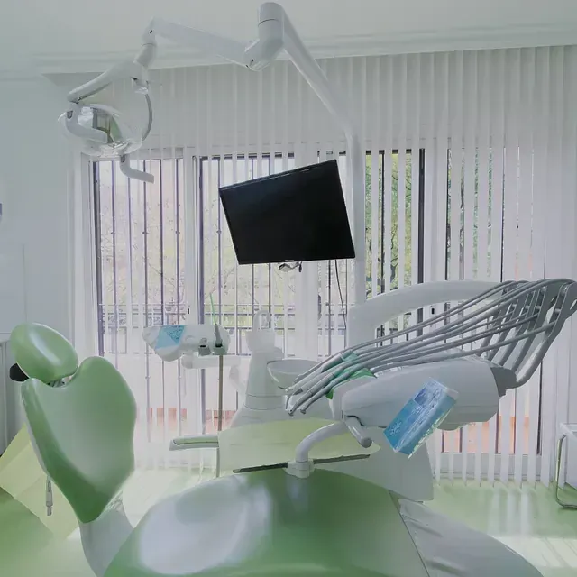 Un consultorio dental con una silla verde y un monitor.