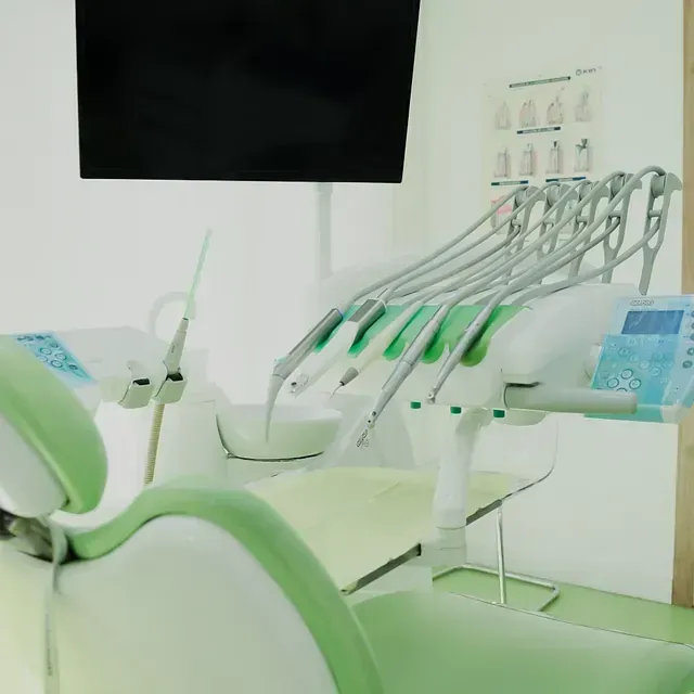 Un consultorio dental con una silla verde y un monitor.