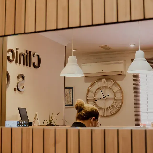 Una mujer está sentada en un escritorio frente a un reloj y un cartel que dice clínica.