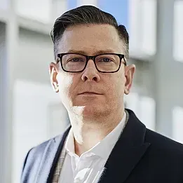 Un hombre que lleva gafas y traje mira a la cámara.