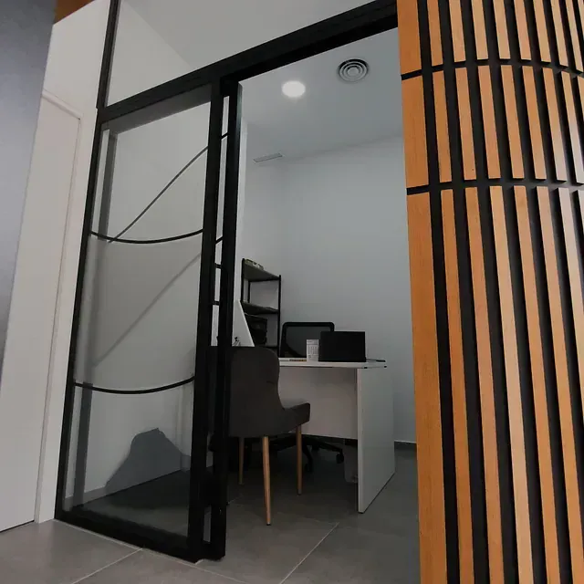 Una puerta corrediza de vidrio se abre a una habitación con un escritorio y sillas.