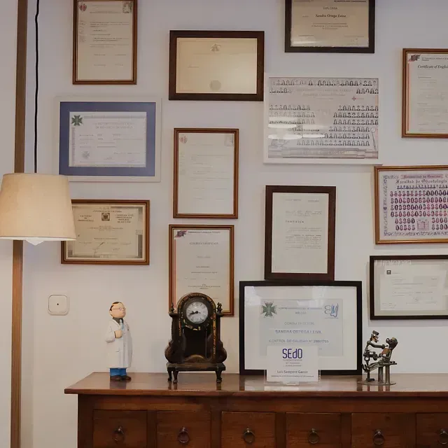 Un reloj está sobre una mesa frente a una pared de certificados.