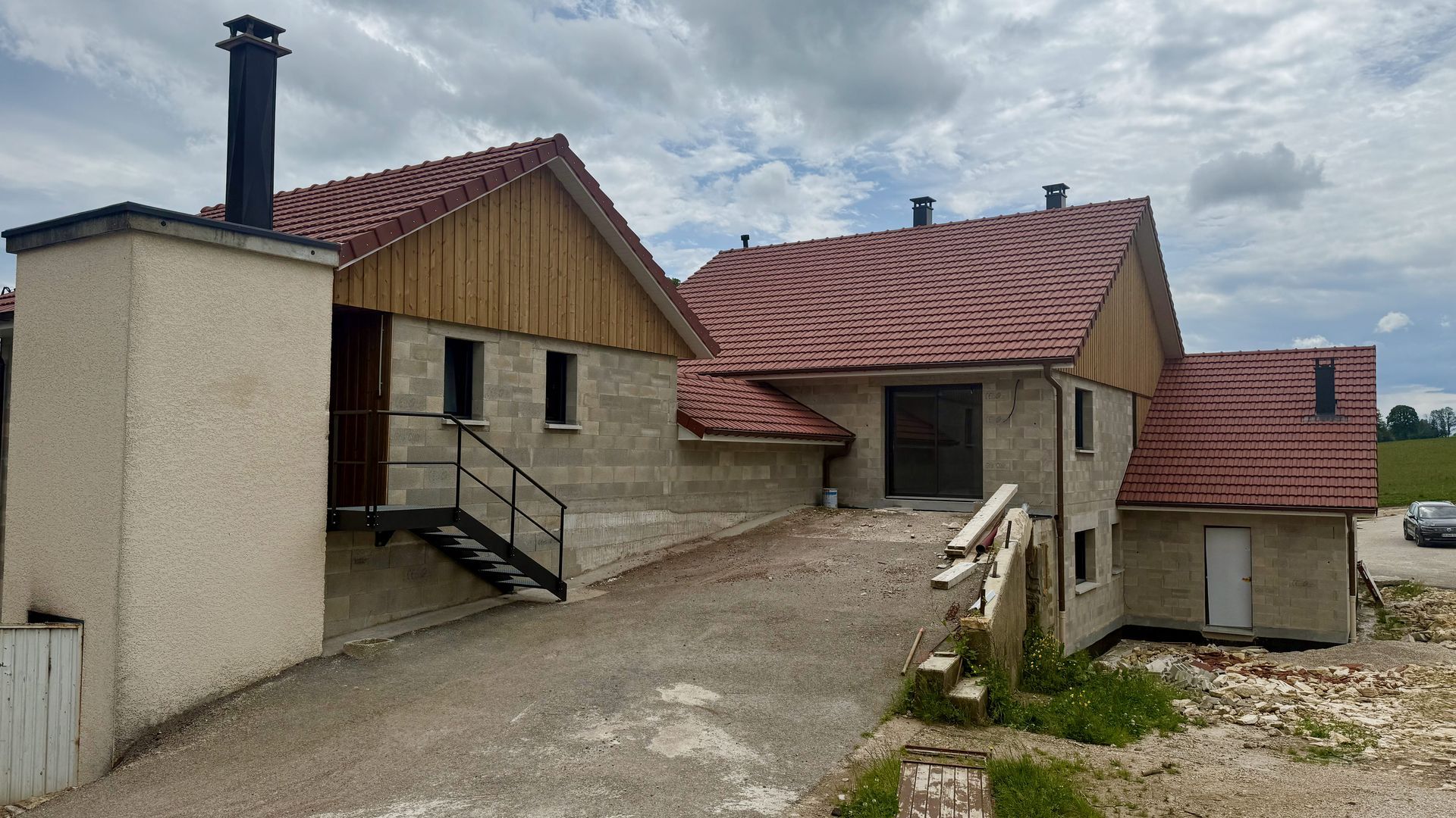 Bâtiment en pierre aux toits rouges et aux cheminées, vu depuis une allée en pente sous un ciel couvert