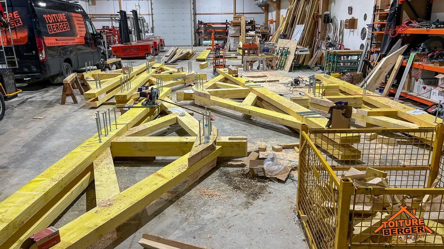 Des chevrons en bois pour charpente dans l'atelier de la société, avec des machines et des outils en arrière-plan