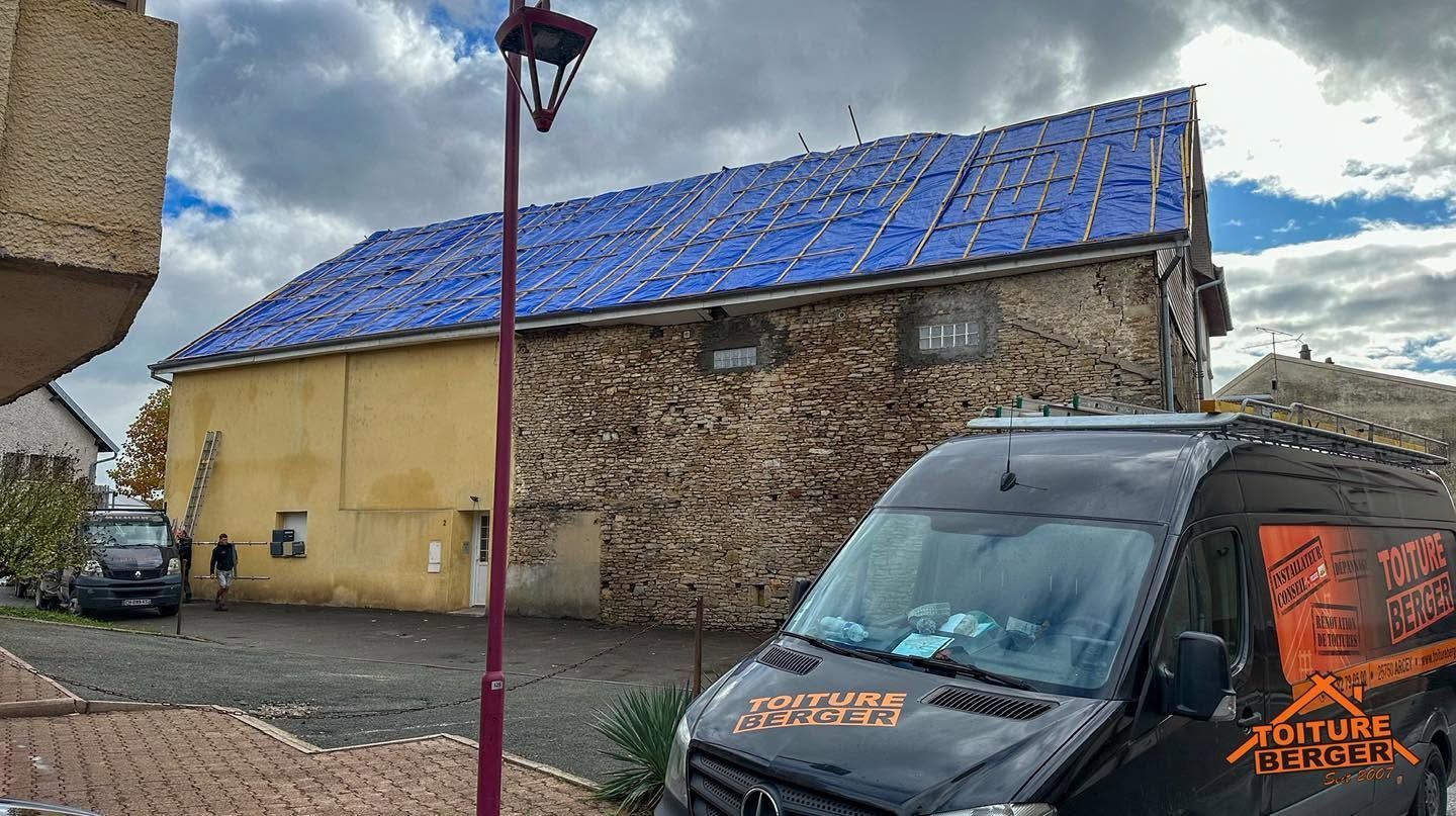 Bâtiment couvert d’une bâche bleue, à côté de camionnettes garées sous un ciel nuageux