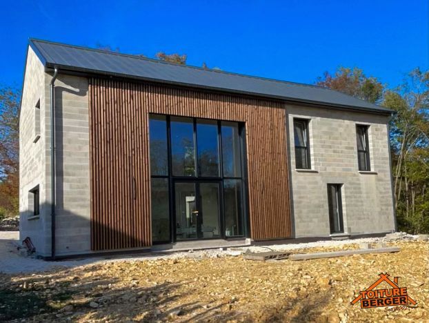 Extérieur d’une maison moderne à étage, avec un bardage en bois, de grandes fenêtres et une cour gravillonnée