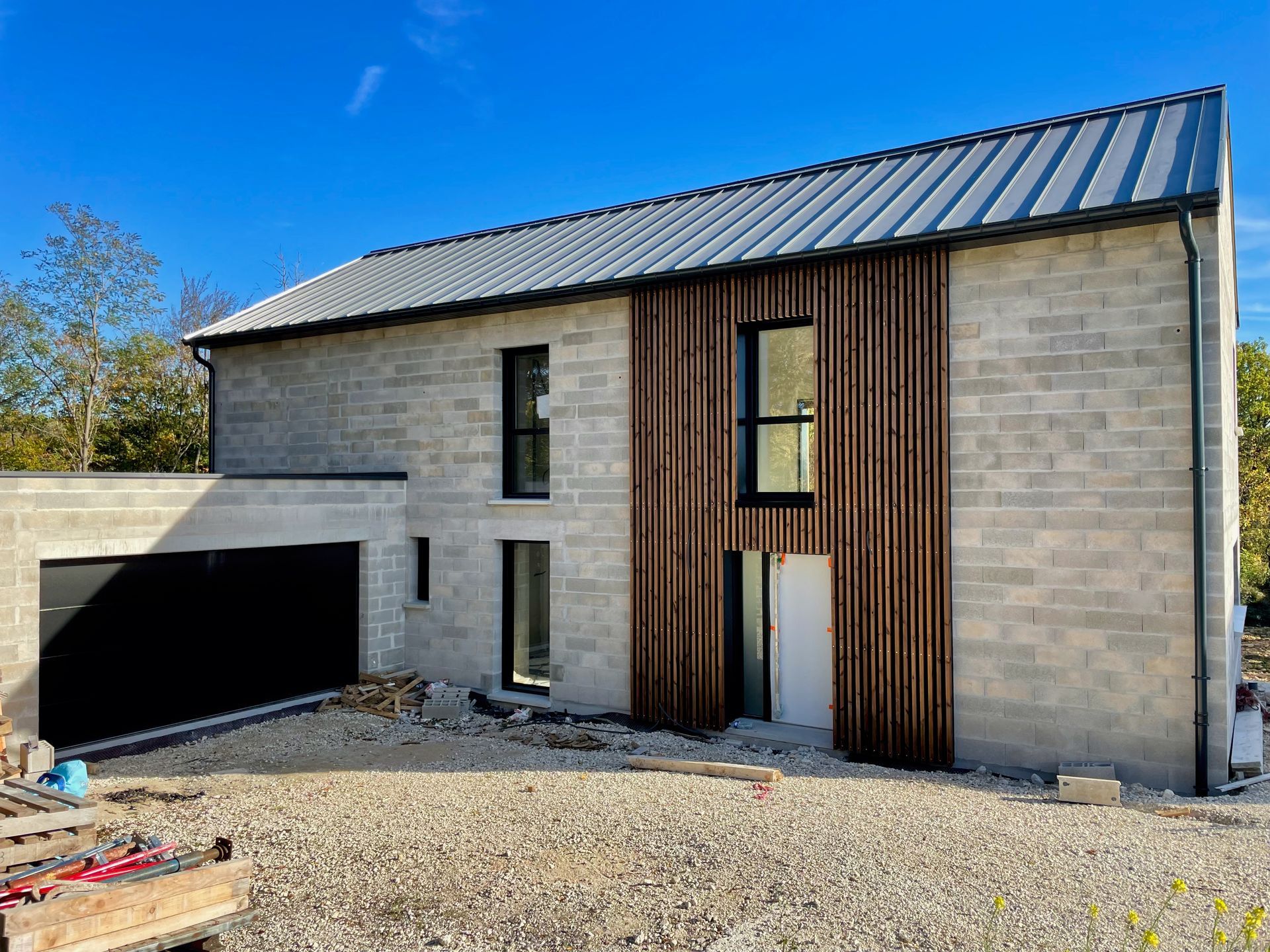Maison moderne à deux étages, en briques claires, avec un toit sombre et un garage attenant, en construction.