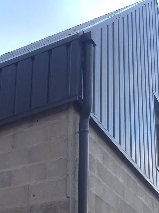 Angle d’un bâtiment en parpaings gris et un bardage en tôle ondulée