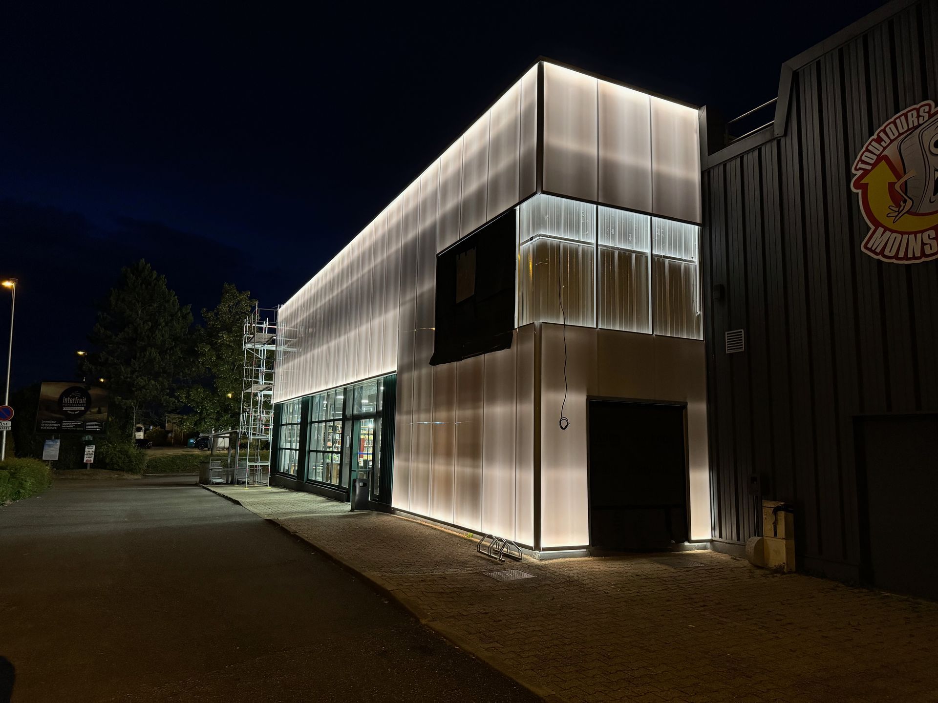 Immeuble moderne avec bardage de façade illuminée, la nuit, au bord d’une rue sombre