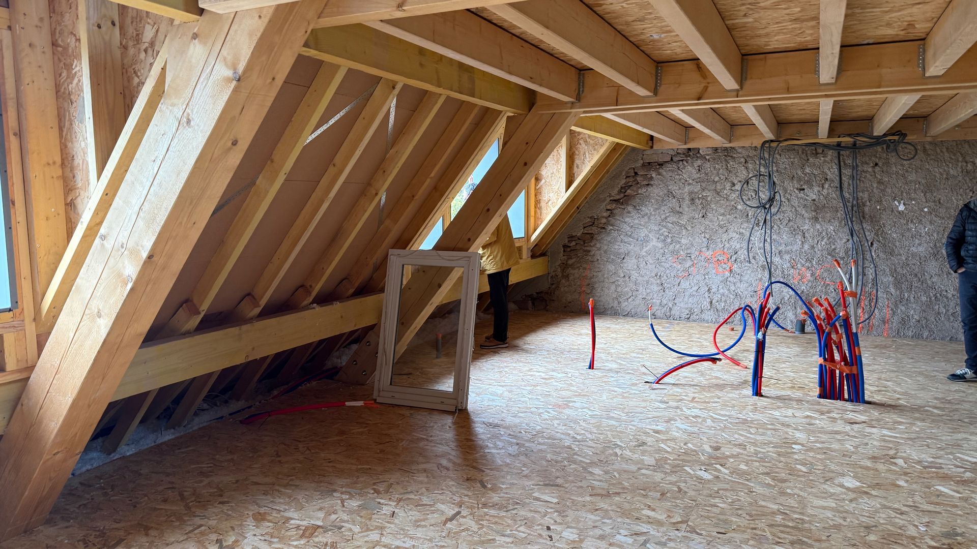 Combles en cours d’aménagement, avec des poutres en bois apparentes et des outils éparpillés sur le sol