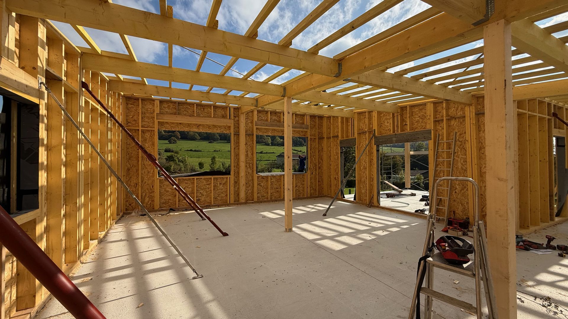 Intérieur d’une maison en bois inachevée, avec une ossature apparente et de grandes fenêtres