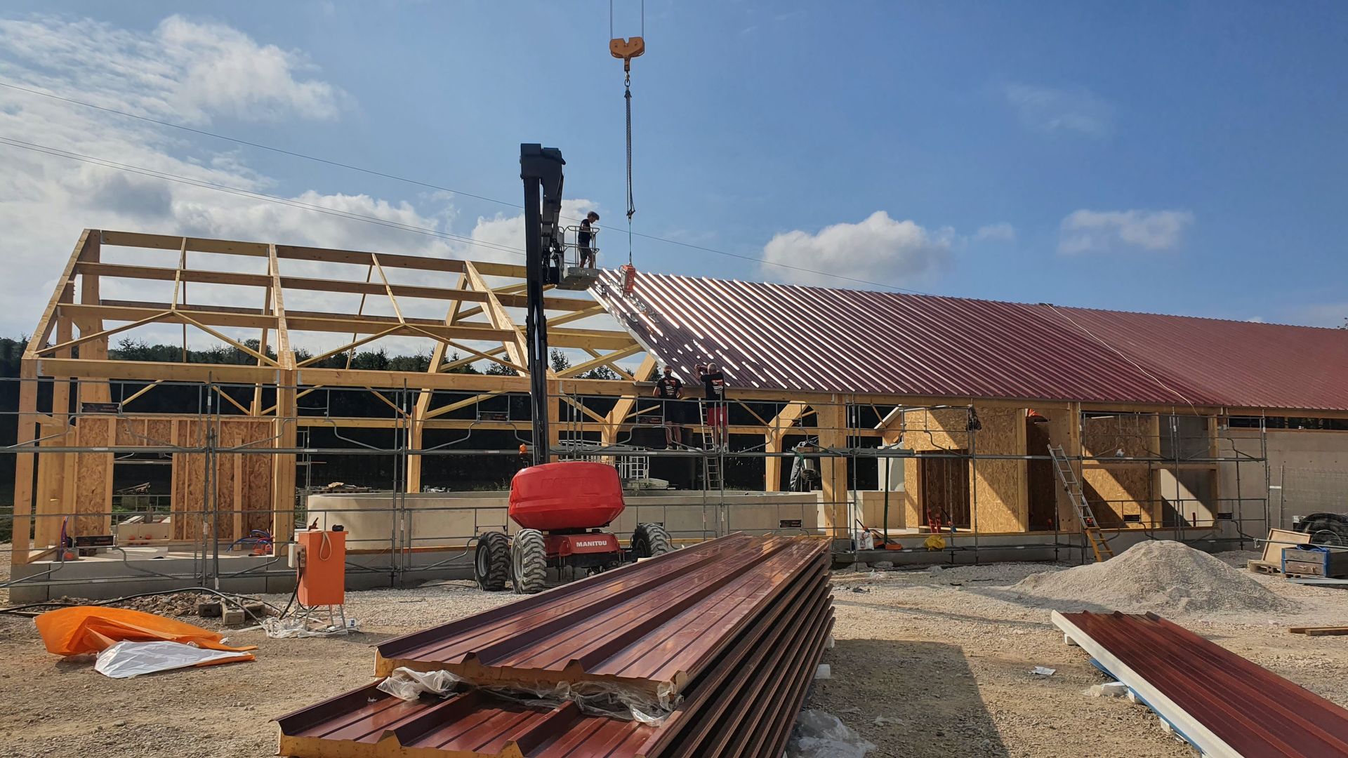 Chantier avec une ossature métallique, des panneaux de toiture rouges et des ouvriers sur un bâtiment en construction