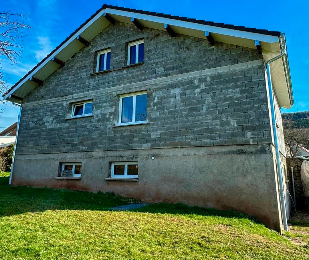 Maison en pierre avec un toit en pente, de petites fenêtres et un jardin herbeux sous un ciel bleu
