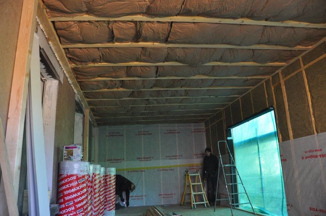Intérieur en cours de construction, avec une isolation apparente, des matériaux empilés et une échelle près d’un mur