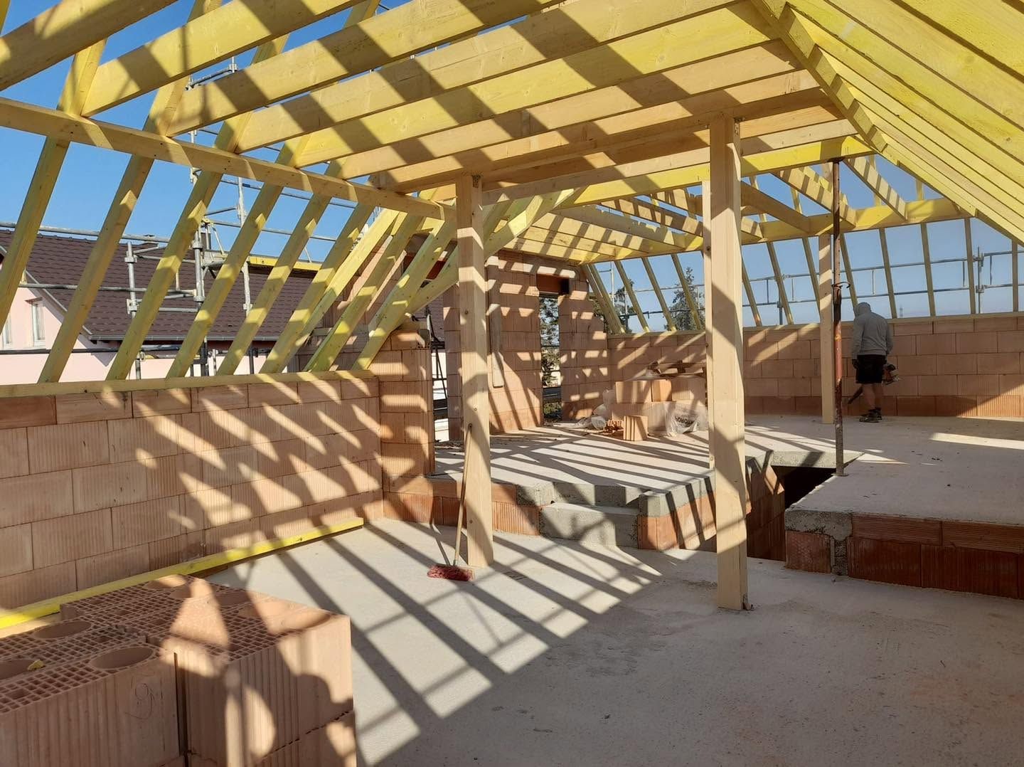 Charpente de toit en bois brut baignée de soleil, projetant des ombres rayées à l’intérieur d’un bâtiment en construction.