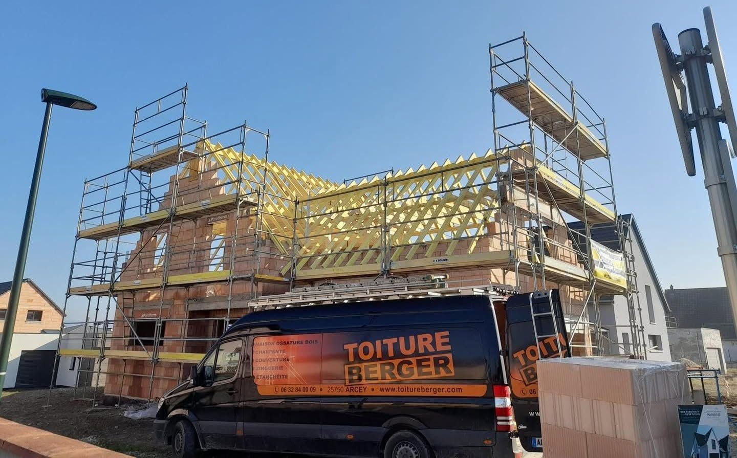 Un échafaudage autour d’un bâtiment en construction, à côté d’une camionnette garée dans une rue ensoleillée