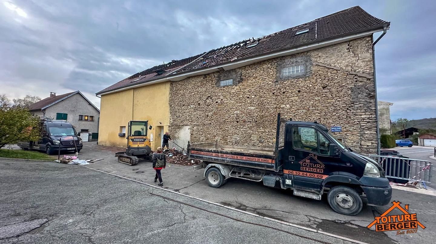 Ancien bâtiment en pierre avec une annexe jaune, un camion et un ouvrier sur un terrain gravillonné