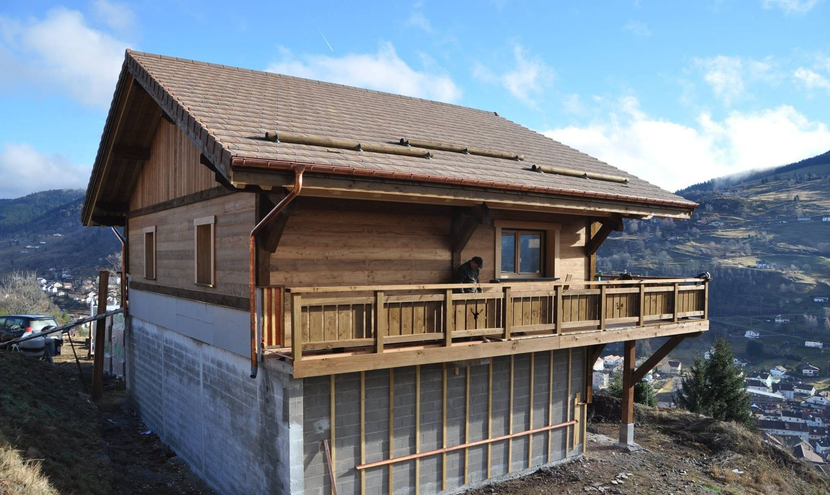Chalet en bois avec balcon sur un flanc de montagne enneigé sous un ciel bleu