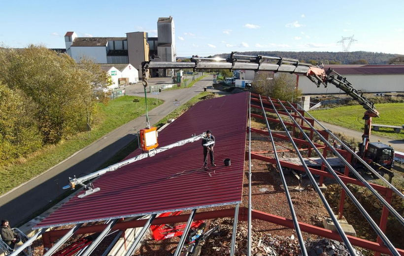 Toiture en cours de réparation avec une sous-couche rouge et des ouvriers sur un chantier, dans un environnement industriel