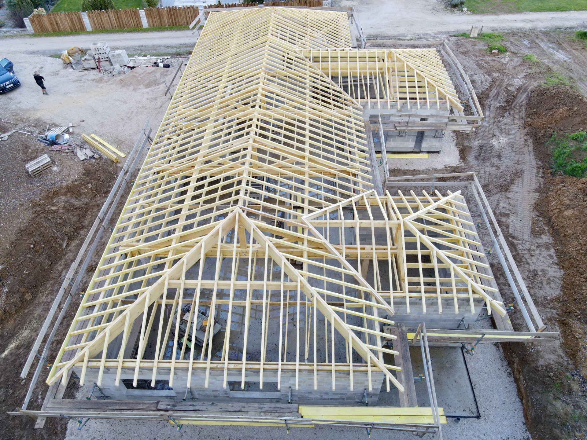 Vue aérienne d’une maison en construction, avec une charpente de toit jaune et des fondations en béton tout autour