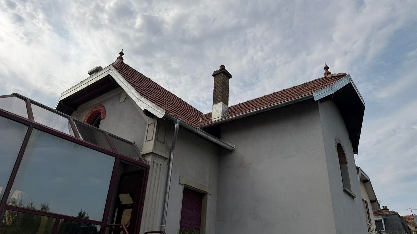 Maison blanche au toit de tuiles rouges et aux cheminées, sous un ciel nuageux
