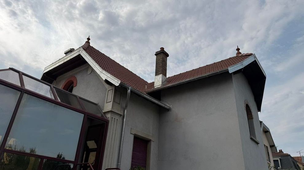 Maison blanche aux toits de tuiles rouges et aux cheminées, sous un ciel nuageux, vue d’en bas